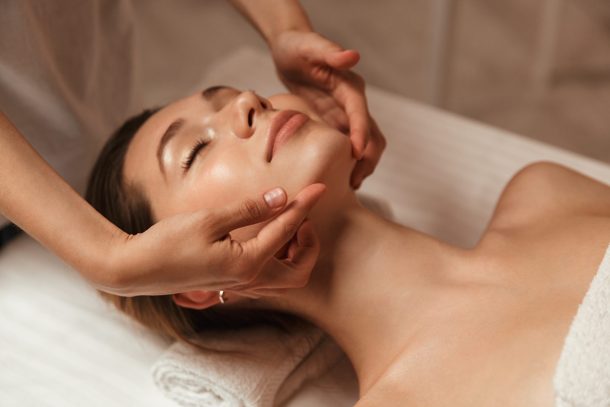 Esthetologist's hands cradling a client's face during a facial treatment