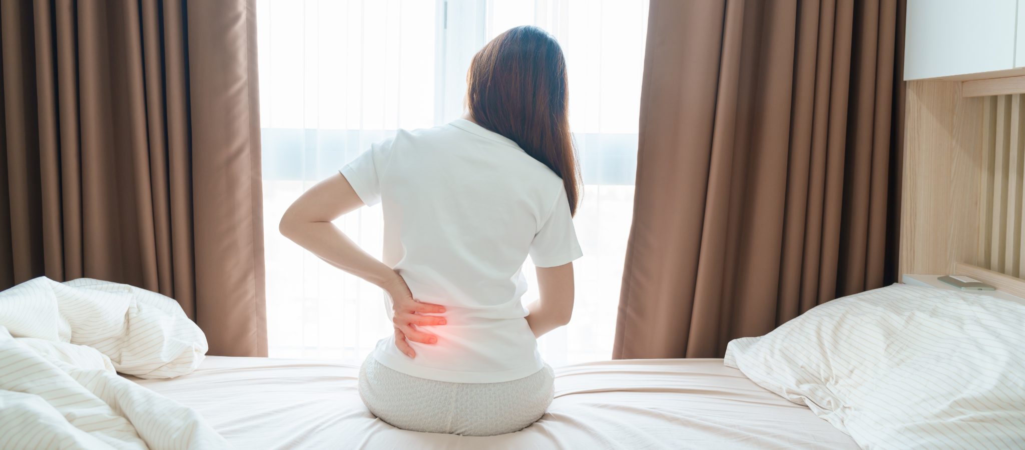 Person sitting on the edge of the bed, holding their lower back where pain radiates