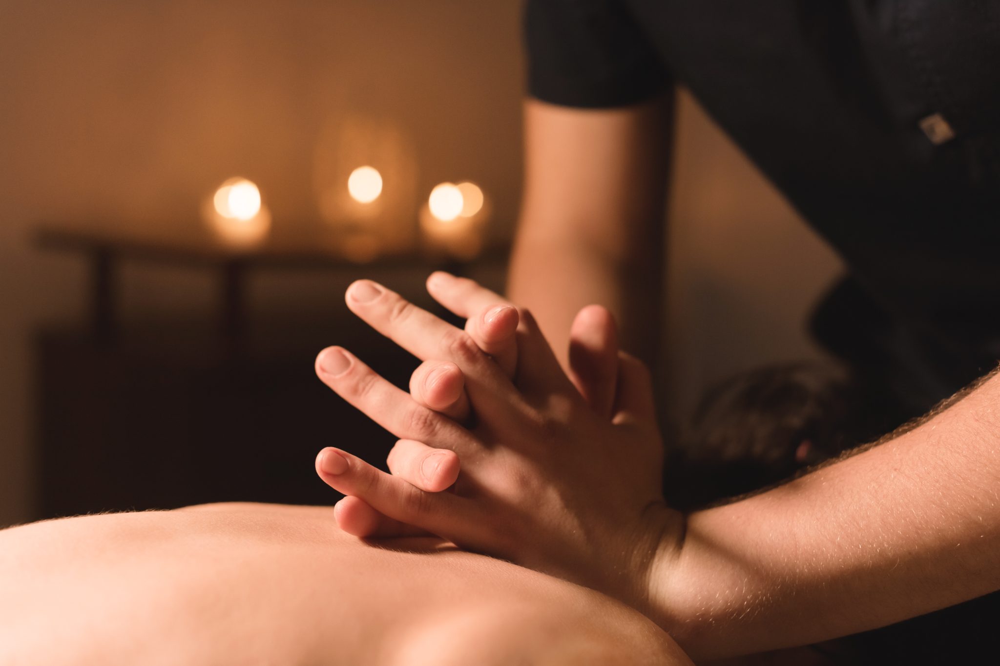 Therapist's overlapping hands applying pressure during a Tui Na massage session, soft candlelight